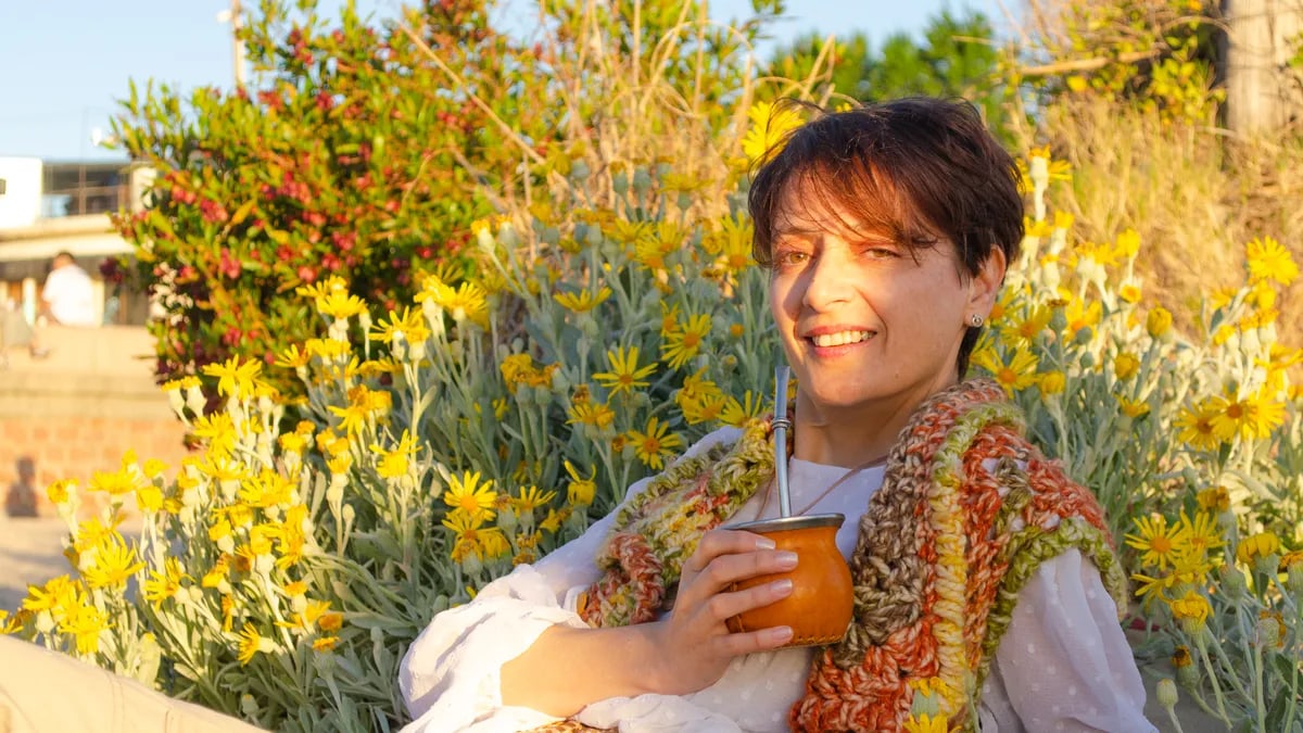 A woman smiles while drinking traditional mate among yellow flowers in Montevideo.